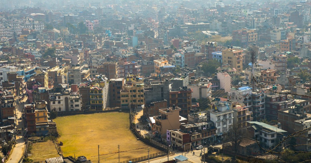 Elevated daytime view over Kathmandu's dense urban landscape, mid-rise buildings and streets stretching to the horizon