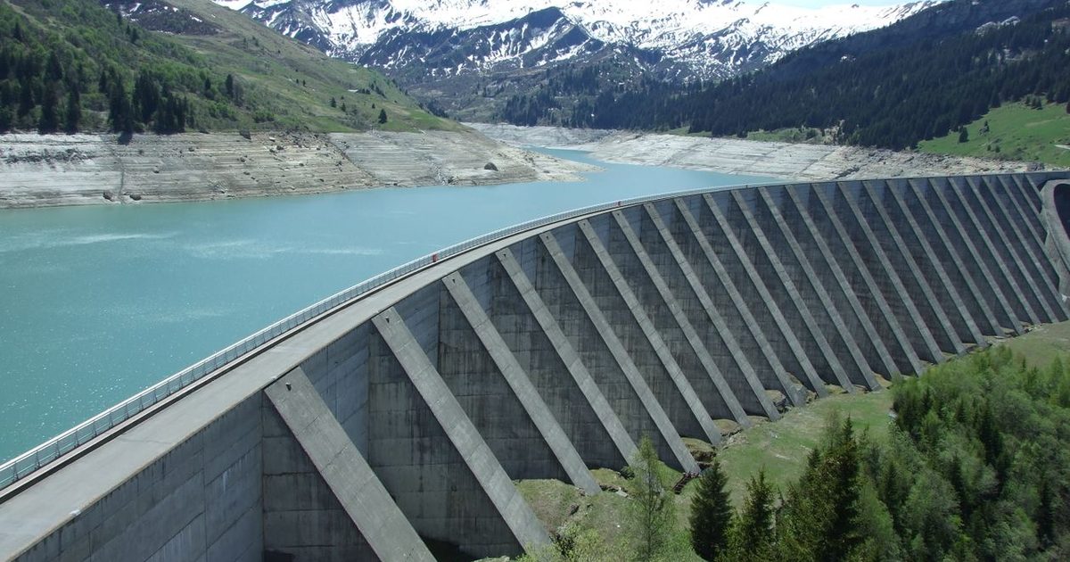 A concrete hydropower dam holding back a reservoir against snow-capped mountains (representative photo)