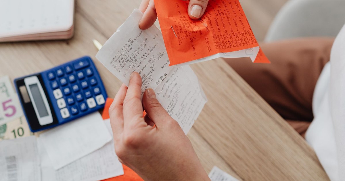 Hands holding receipts over a desk with a calculator, laptop and notes (representative photo)